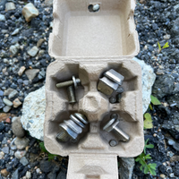 A 4-egg natural pulp carton used to organize nuts, bolts, and screws. Background is gravel.
