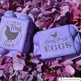 Two purple pulp stamped 6-egg cartons closed, on top of purple flowers. 