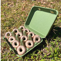 An army green paper pulp 12-Egg carton filled with mini donuts. Carton is sitting outdoors on the grass.