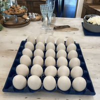 A blue plastic washable, stackable, reusable, 30-cell egg tray filled with medium eggs, sitting on a rustic kitchen table
