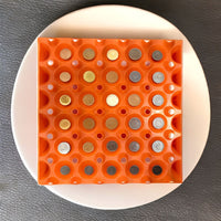 An orange plastic, stackable, reusable tray with 30-cells used for organizing a coin collection.